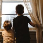 boy and girl standing near window looking outside